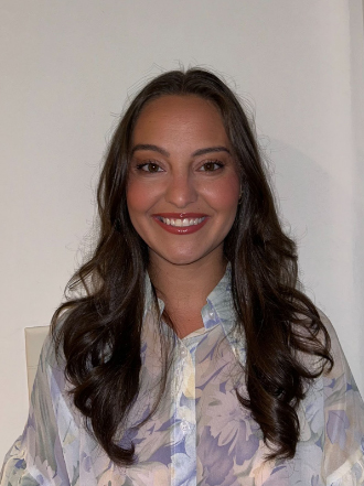 A brunette person with wavy hair in a pastel colored blouse.