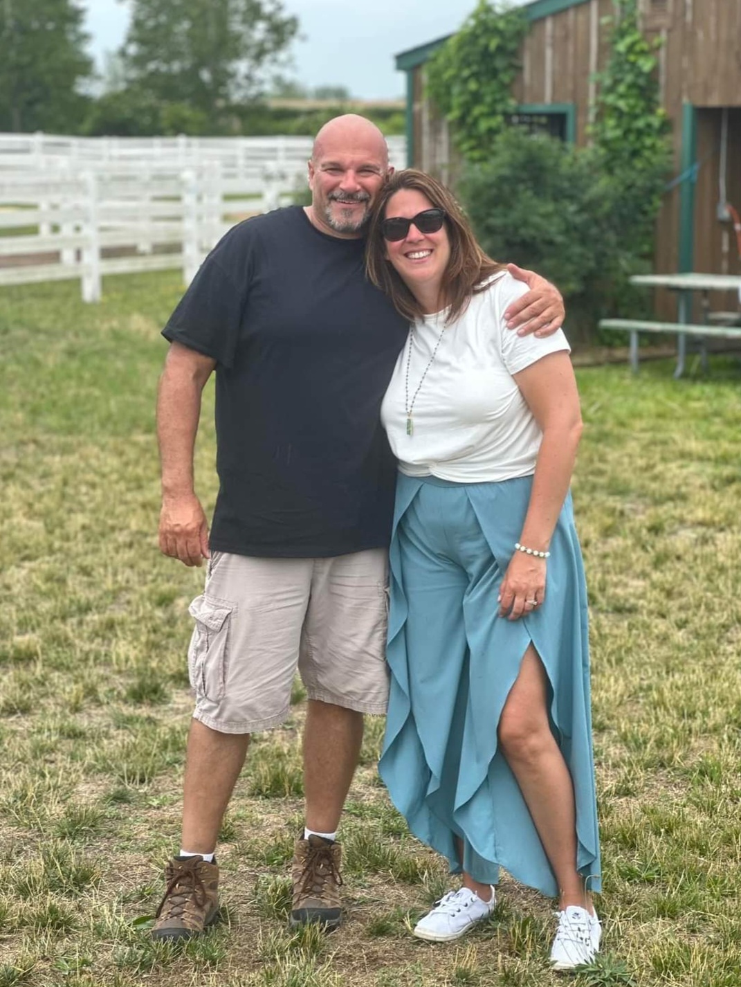 Two people embracing outside a wooden horse barn at an outdoor event.