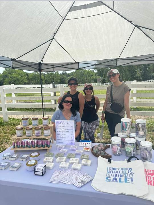 Four people wearing sunglasses behind a table with products at an outdoor popup shop event.